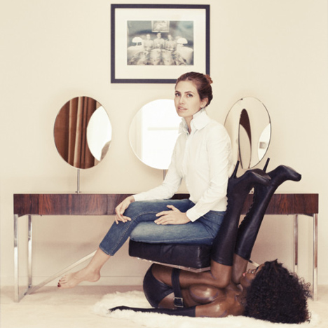 Russian gallerist Dasha Zukhova sitting on a chair in the form of an inverted semi-naked black woman