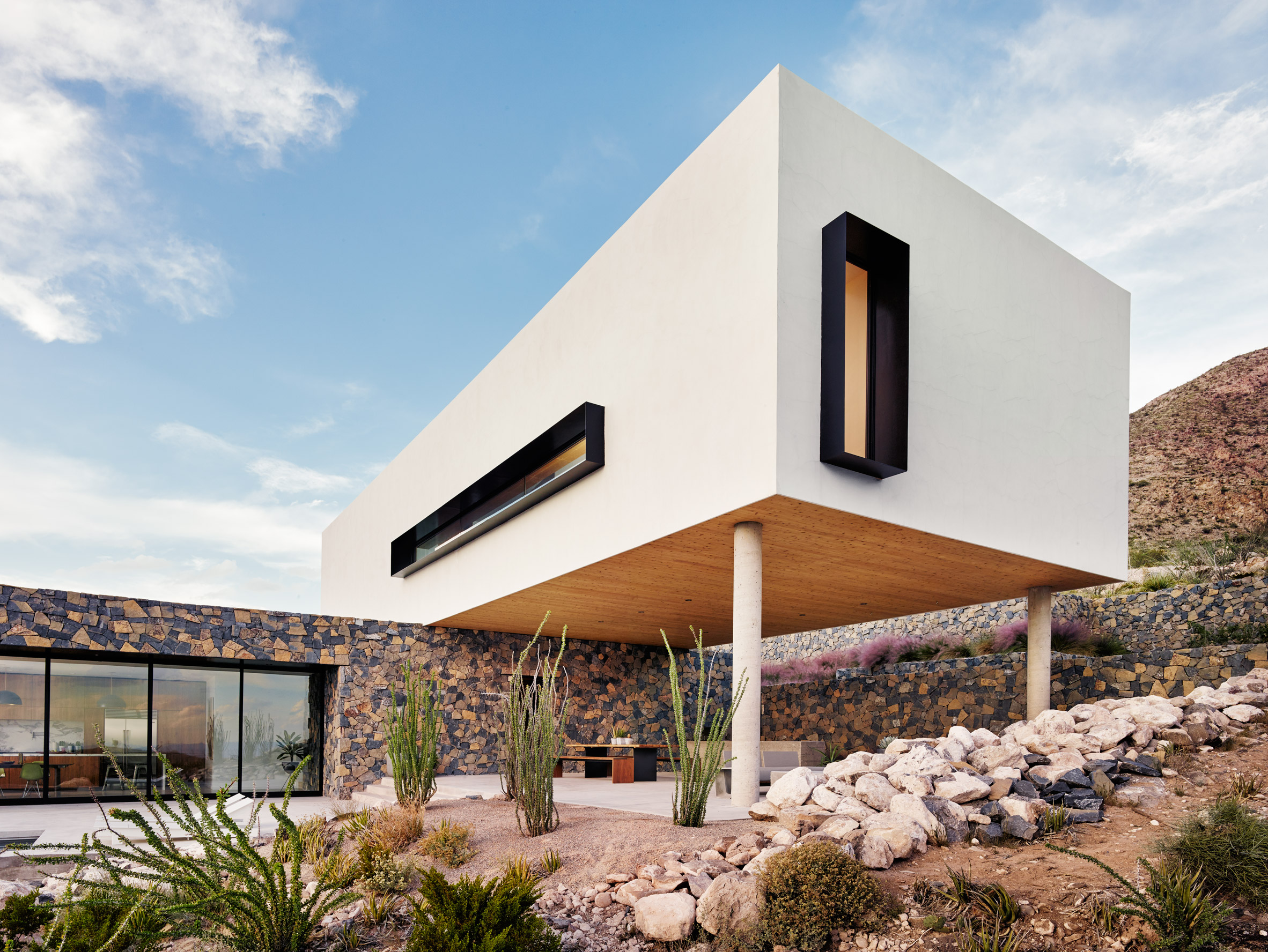 Volcanic stone contrasts with white stucco at Texas desert home by Hazelbaker Rush