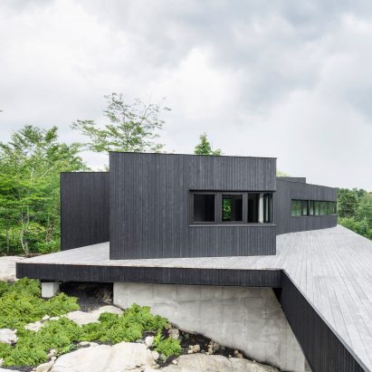Pilotis support black house on Canadian hillside by Atelier General