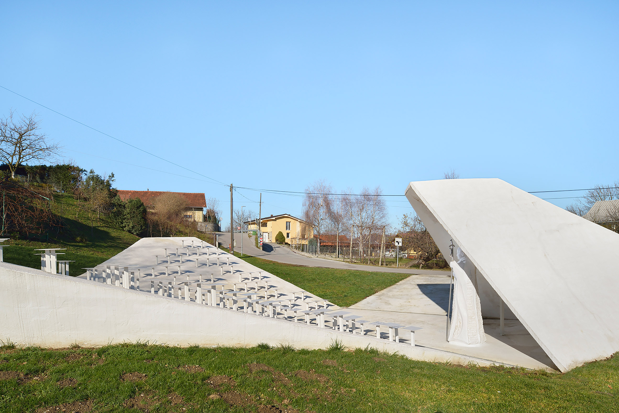Sloping concrete volumes enclose social hub and chapel in a Slovenian village