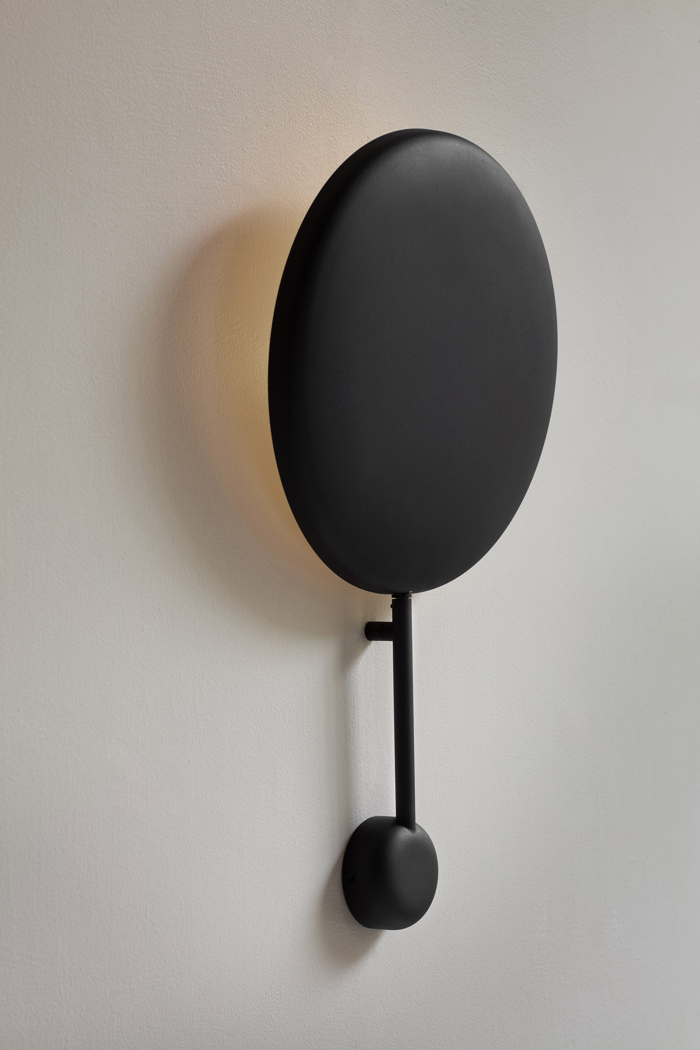 The Ink wall lamp features a concave disc-shaped body with a matt black finish