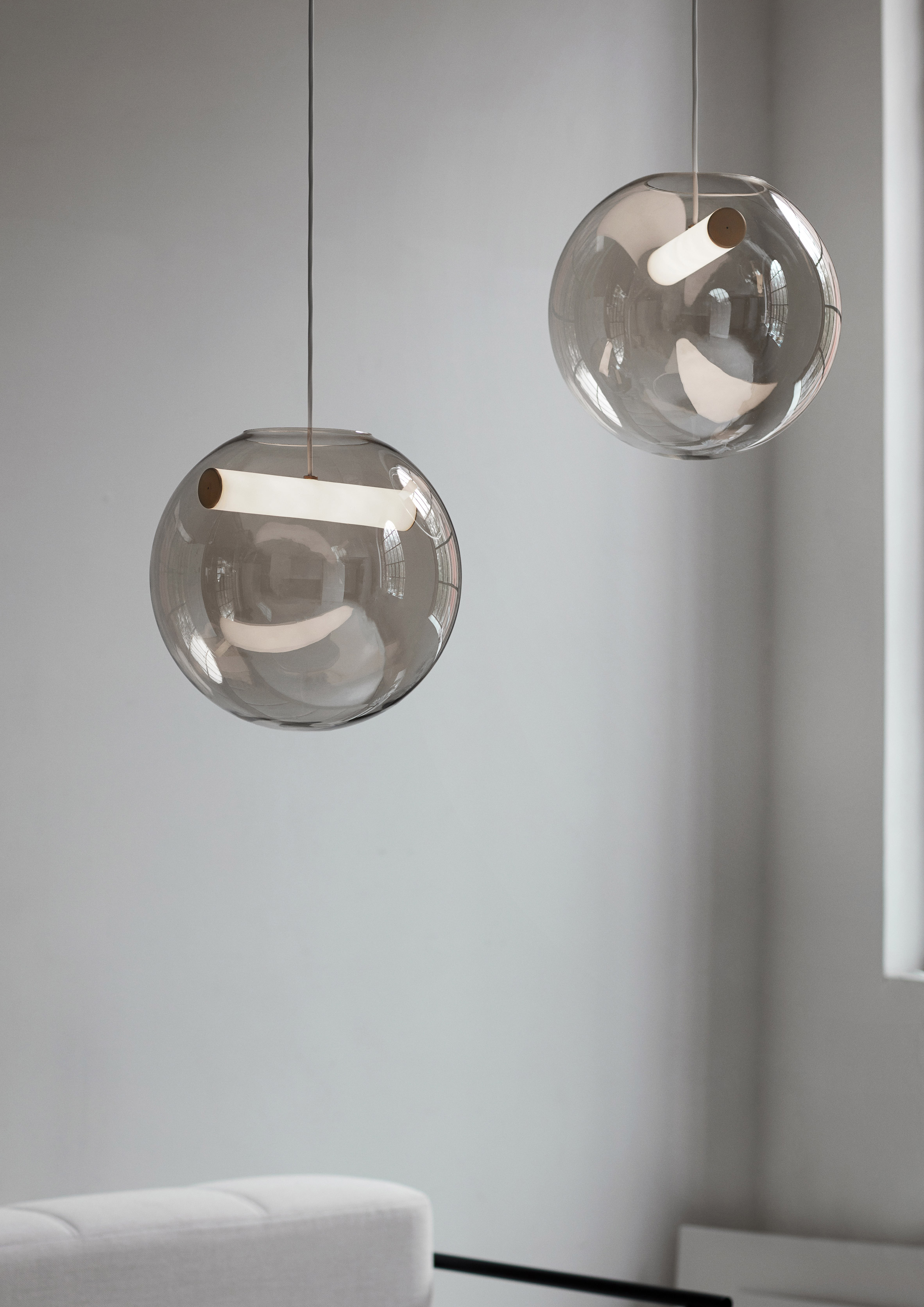 The Reveal pendant lamp by Silje Nesdal comprises a hollow sphere of glass, framing a horizontal light suspended on a copper-coated cord.