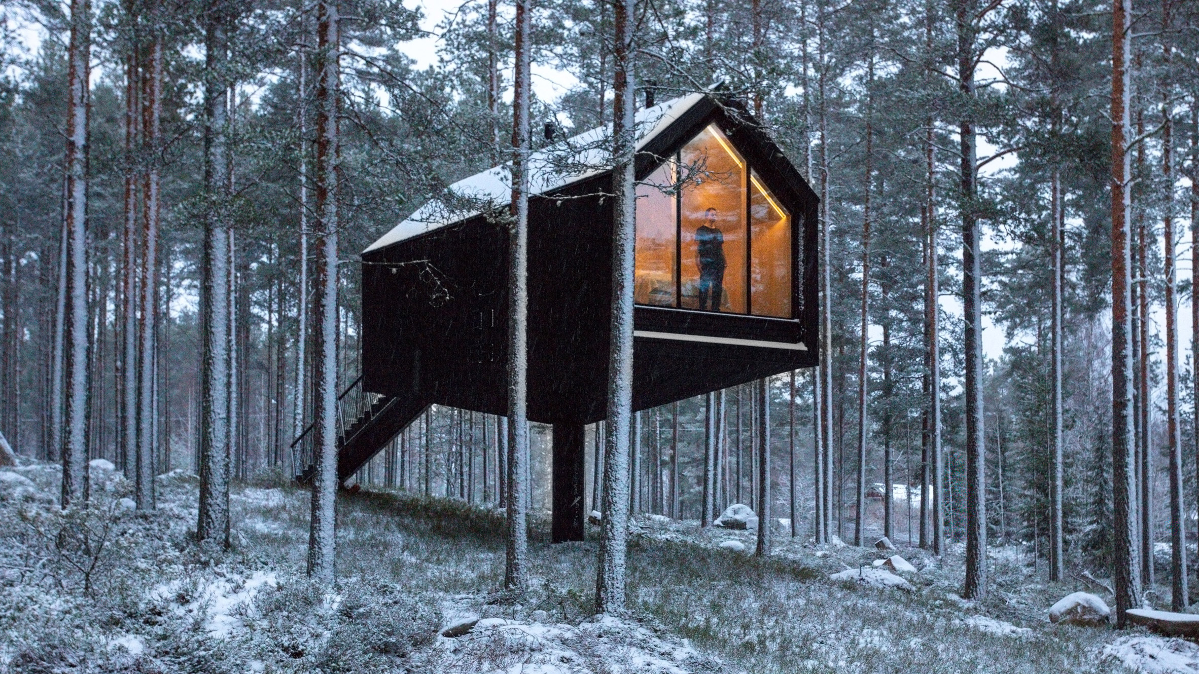 A black-painted cabin elevated in woodland in Finland