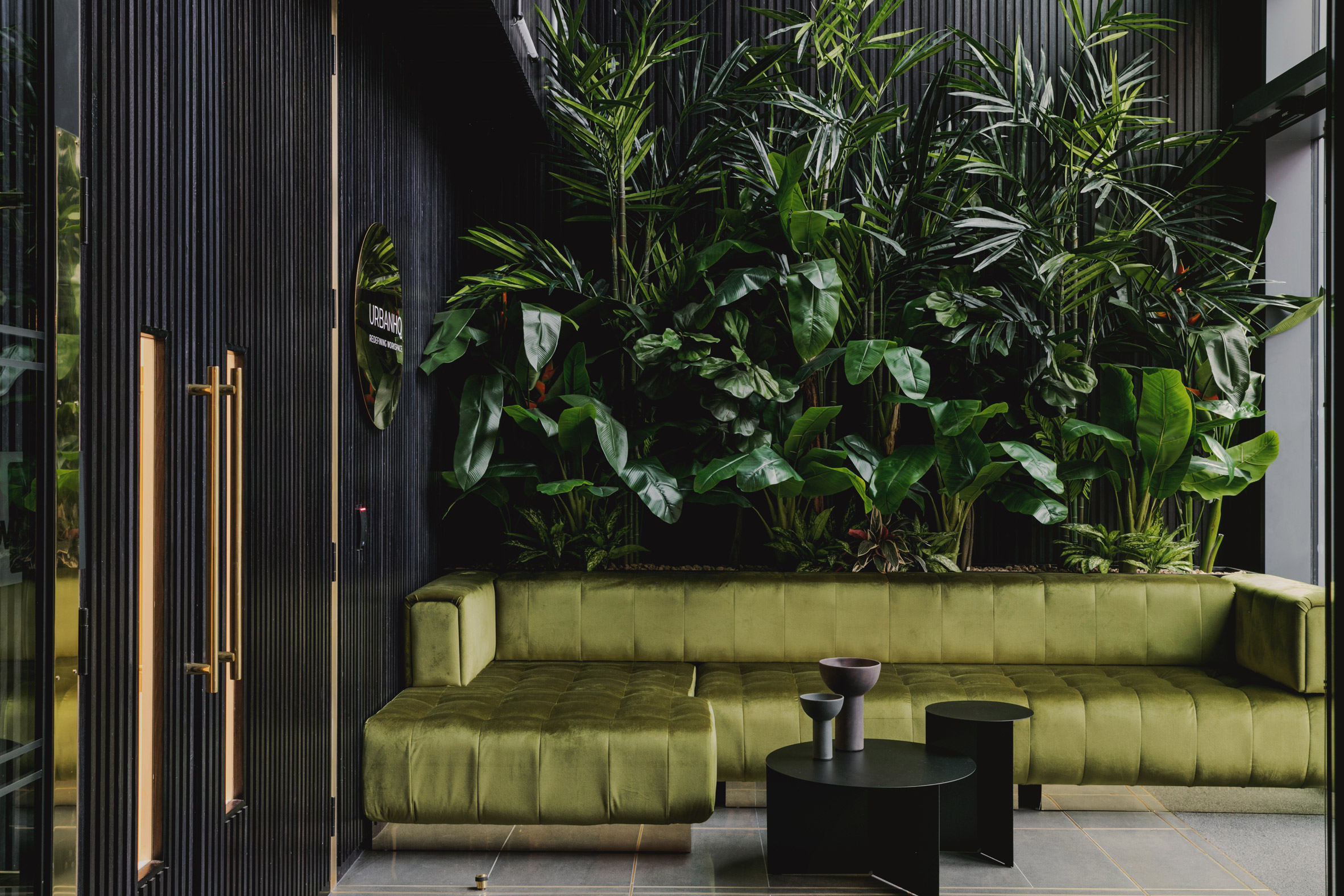 A green sofa in front of a wall of plants