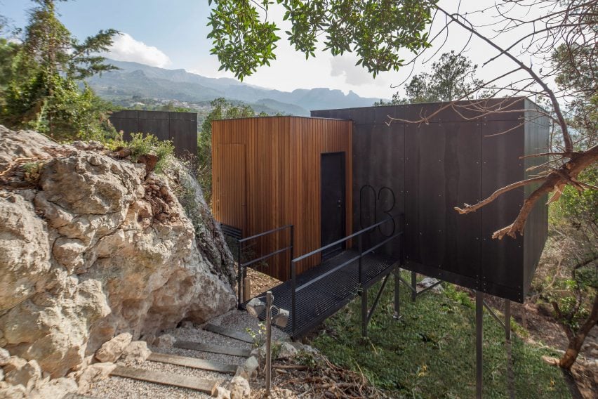 Cabin on stilts accessed by a path along a rocky terrain by Daniel Mayo