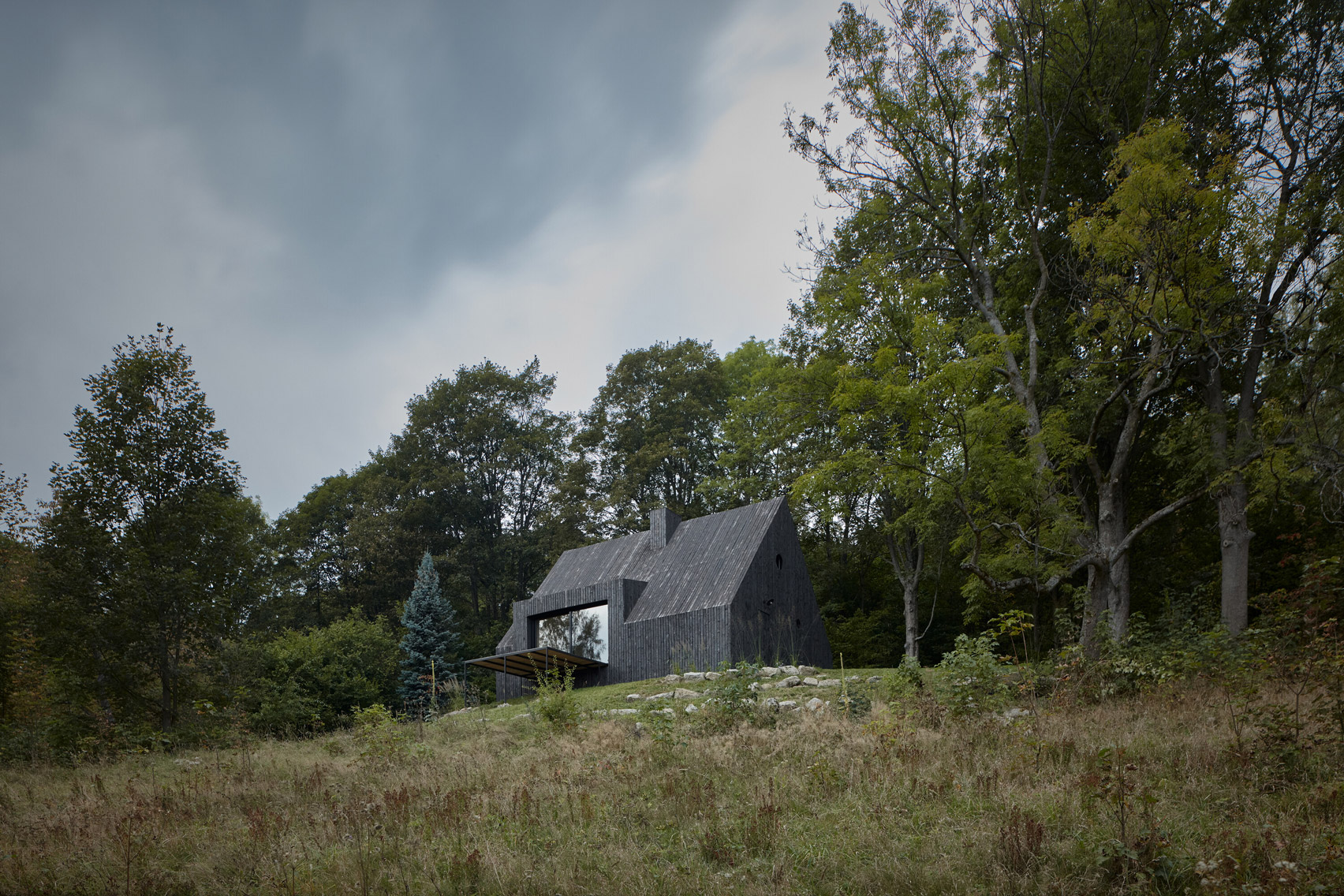 Charred wood cottage sits amongst a wooded area by Mjölk Architekti