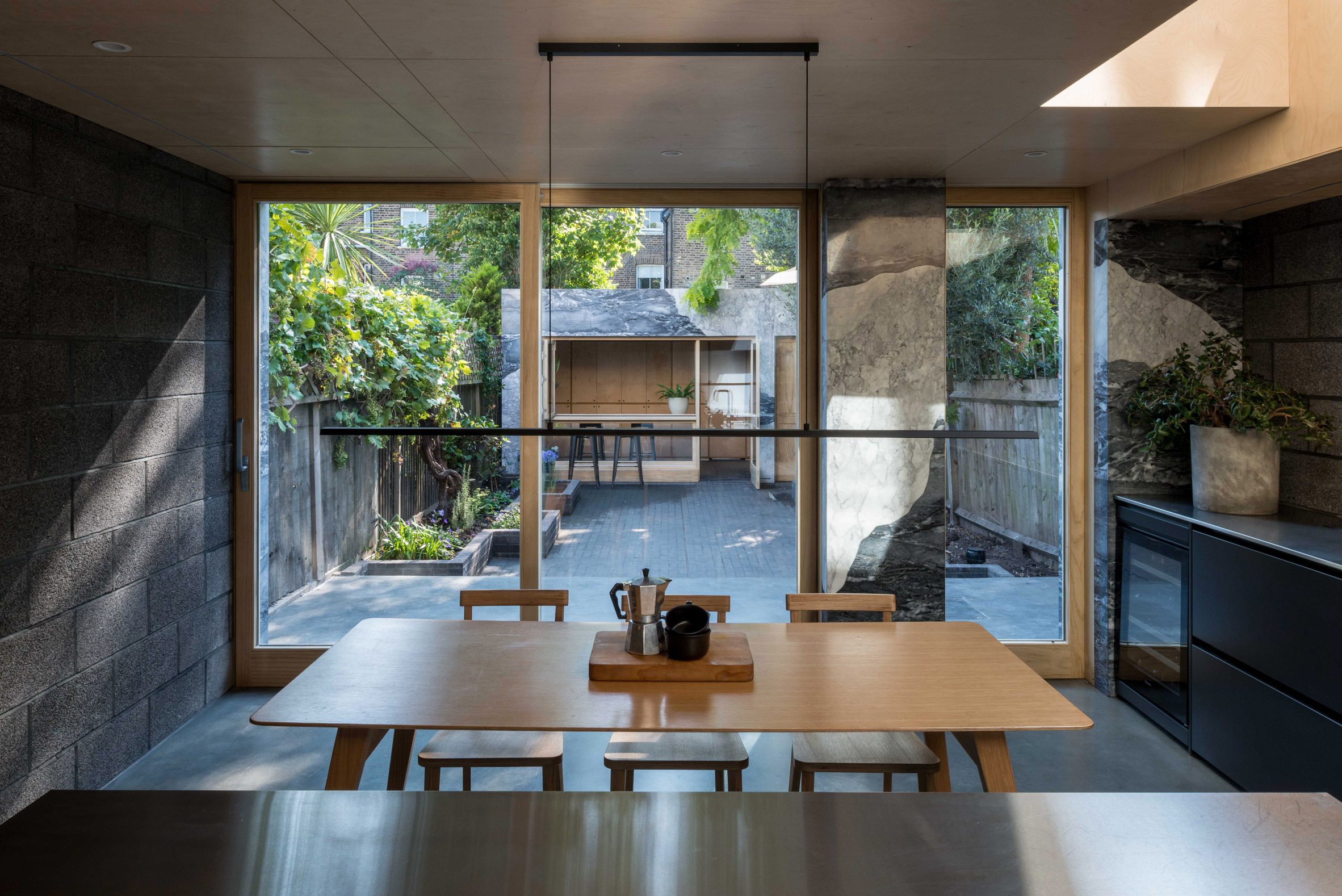 Stainless steel kitchen looking out at garden and marble-clad garden room of Hansler Road extension by Alexander Owen Architecture