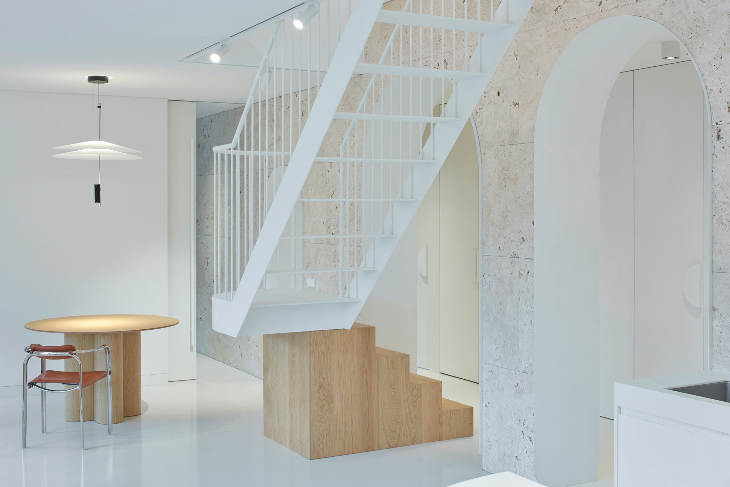 Ground floor of Vilnius apartment by 2XJ with travertine wall and wood and steel staircase