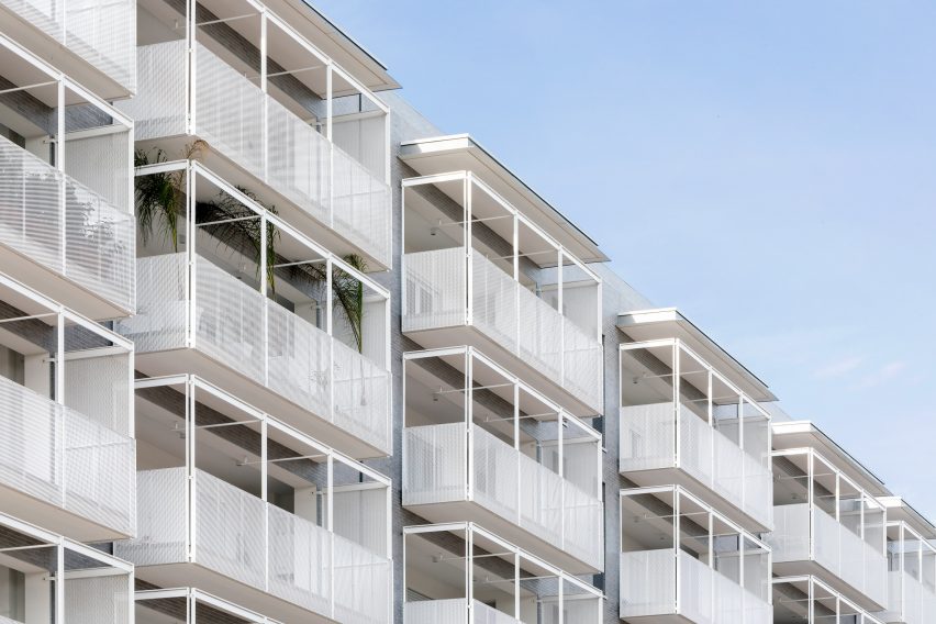 White perforated balconies protrude from the brick