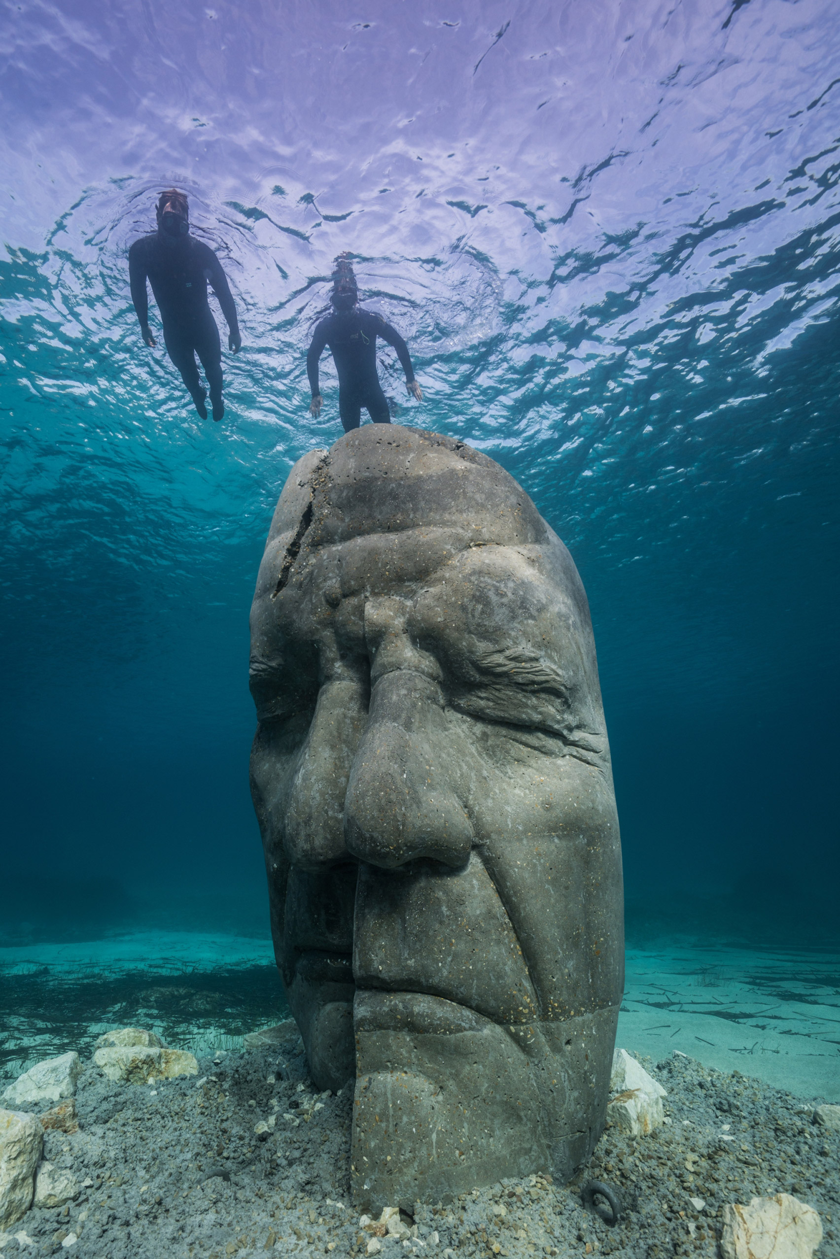 Two snorkelers observing an underwater sculpture of a human face