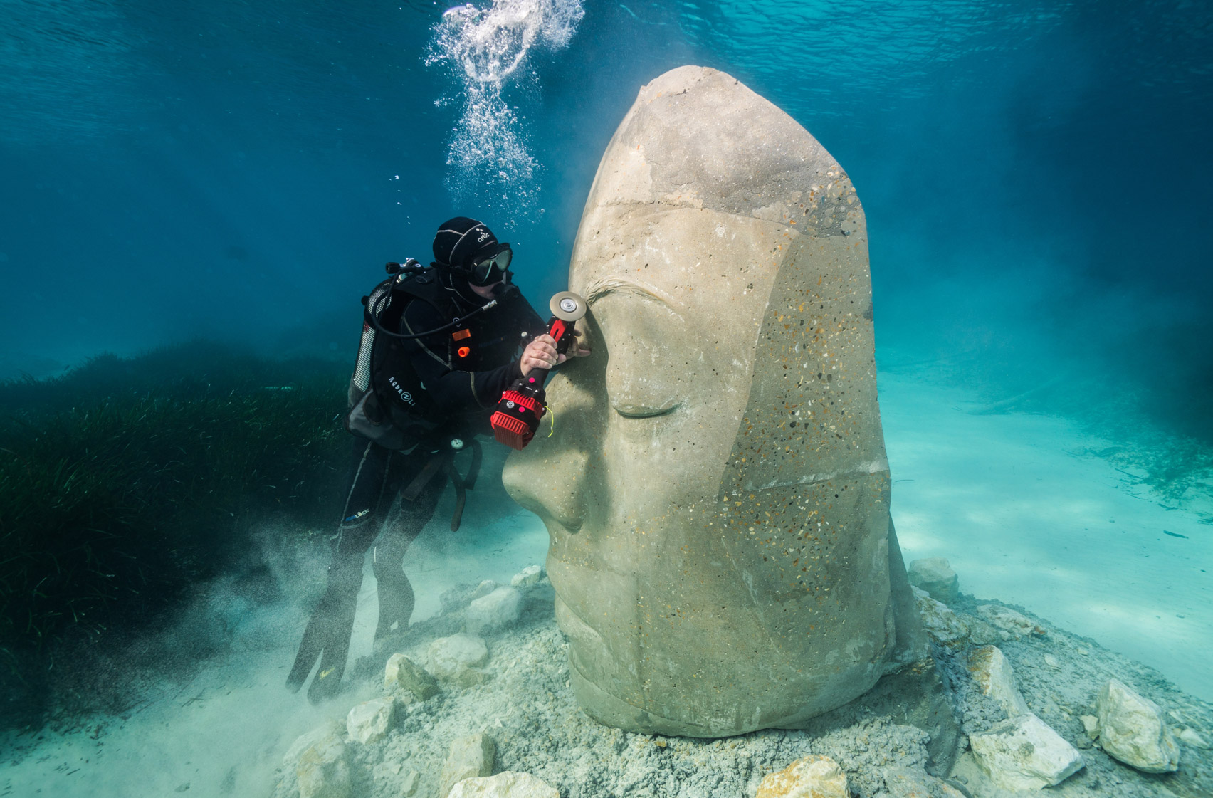 A diver carving a underwater sculpture of a human face