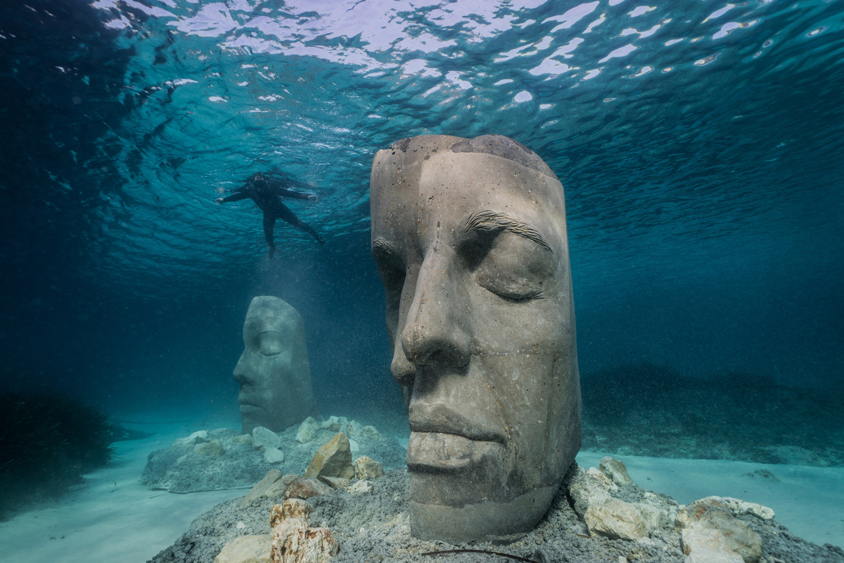 A snorkeler observing two underwater sculptures