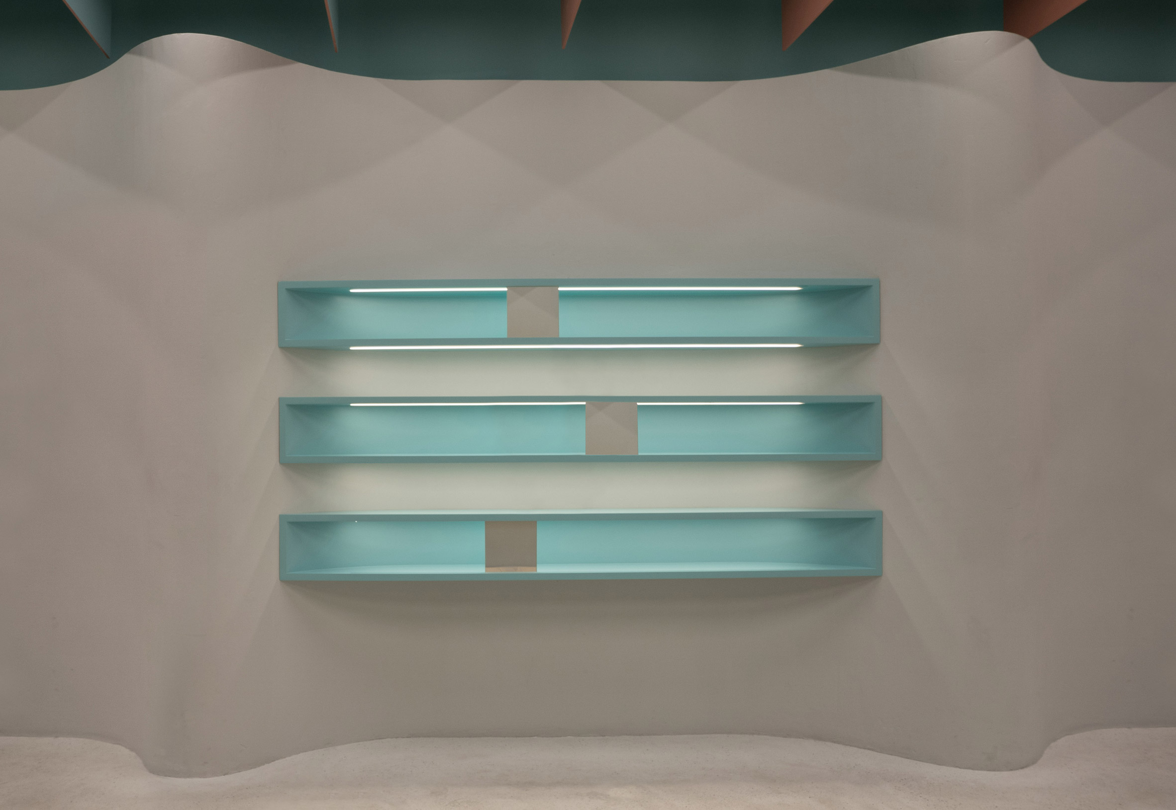 Built-in turquoise shelves in undulating plaster wall of Eyewa store interior