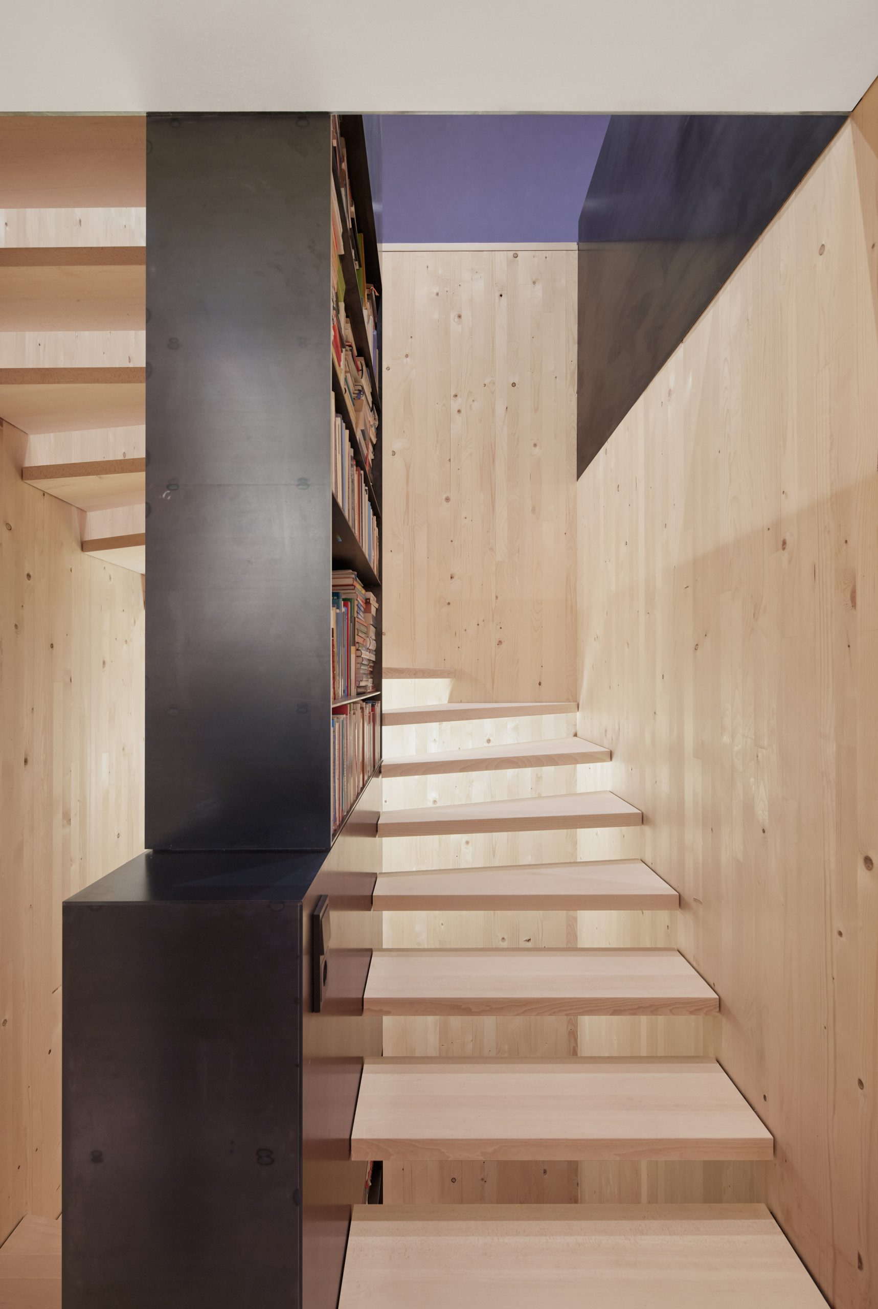 A spruce open-tread staircase with a black steel bookcase