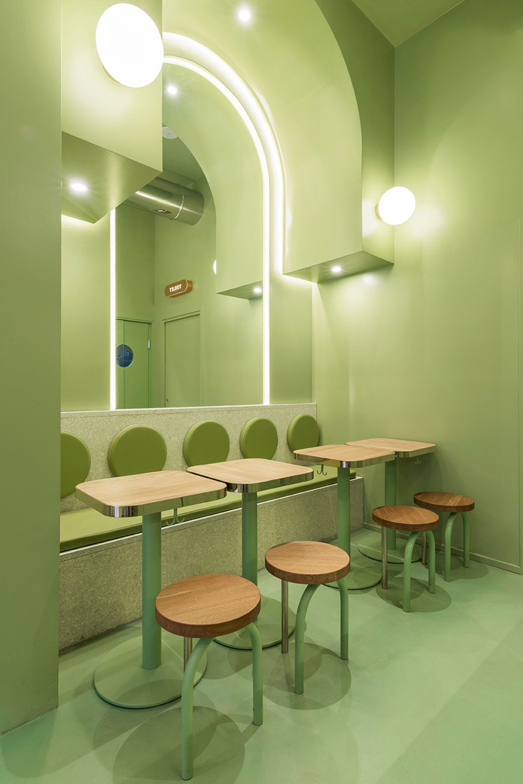 Green seating area with arched ceiling and wooden accents in Milan burger joint