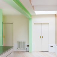 A white kitchen with green structural beams and a wooden floor