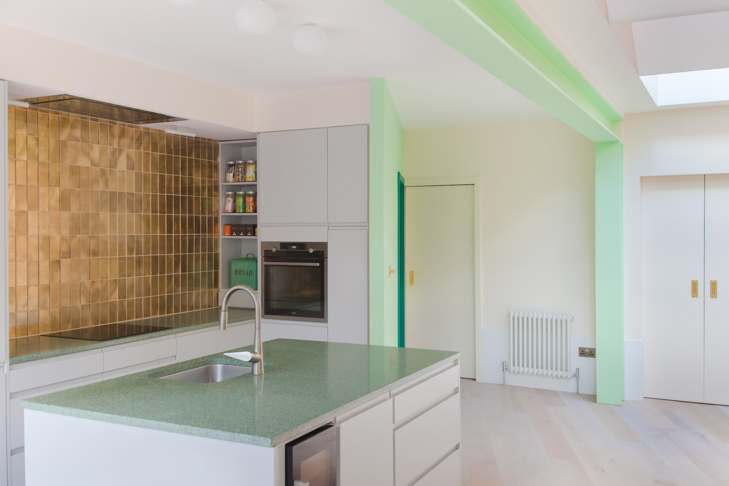 A bright white kitchen with green and gold detailing