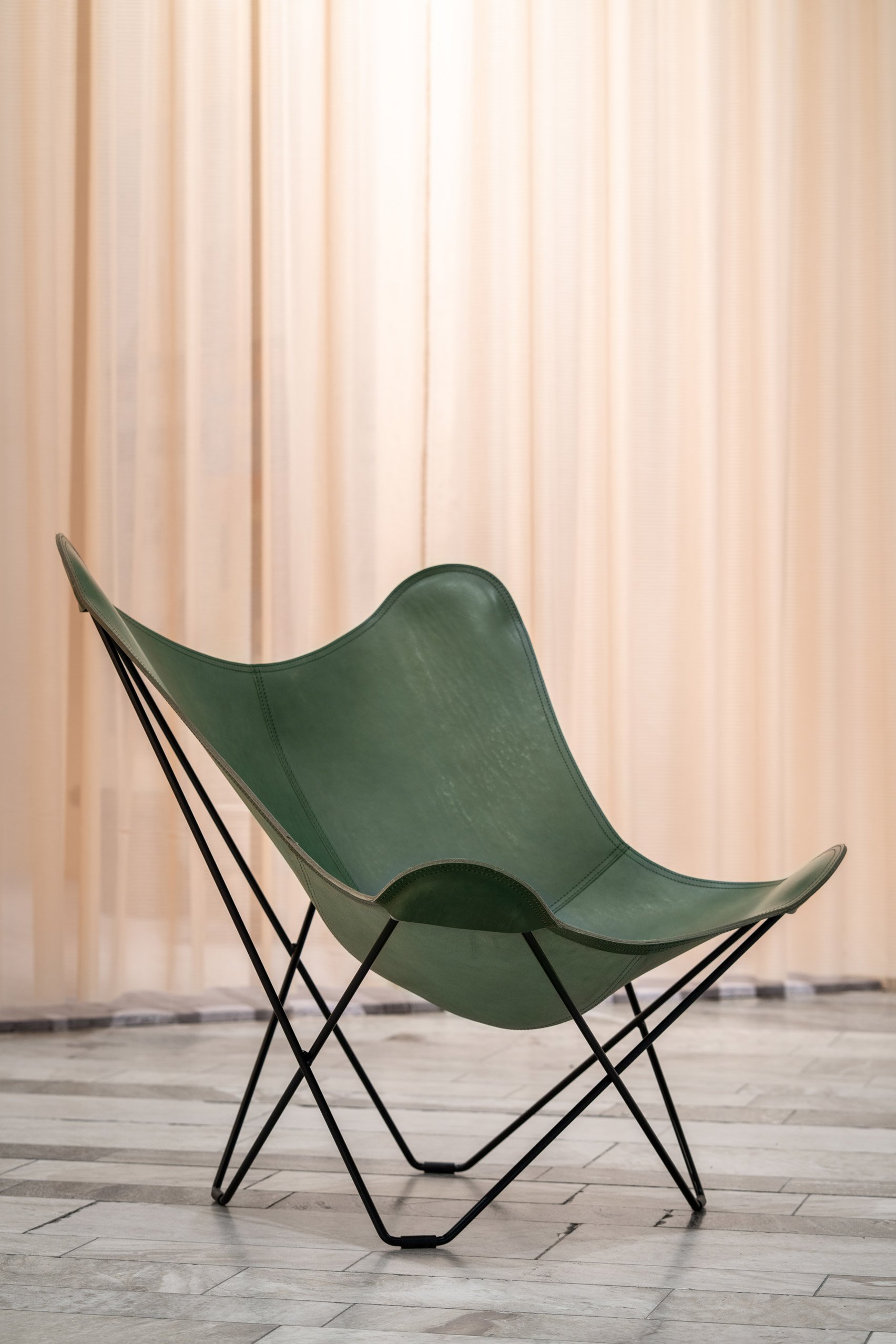 A green leather butterfly chair with a black frame