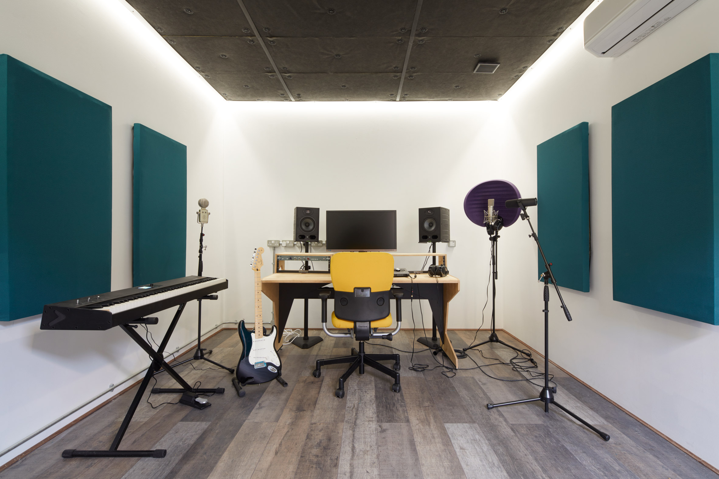 A white-walled music studio with teal acoustic panels