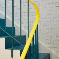 A teal-hued staircase with a yellow banister