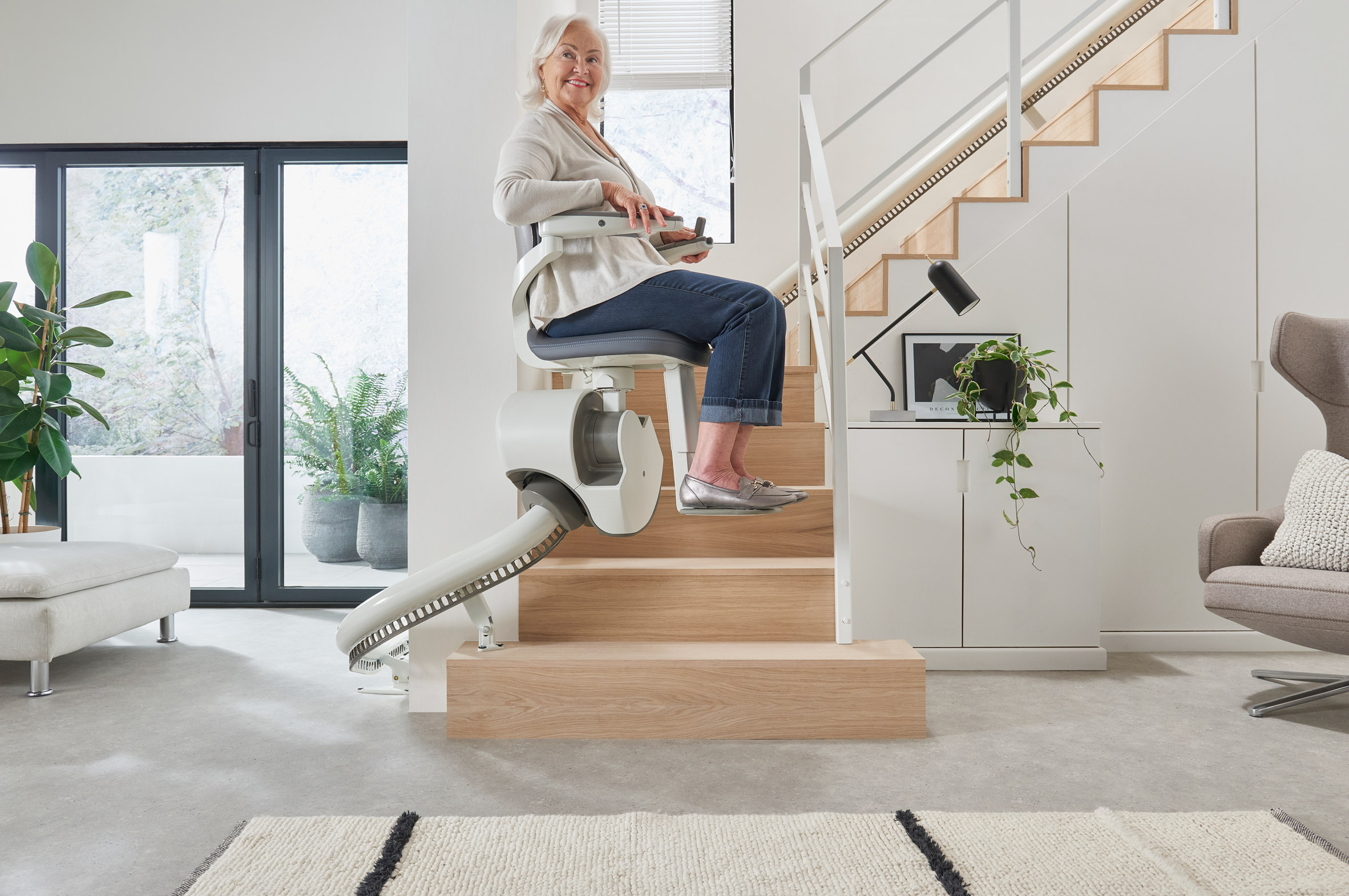 Woman riding Flow X stairlift up a wooden staircase