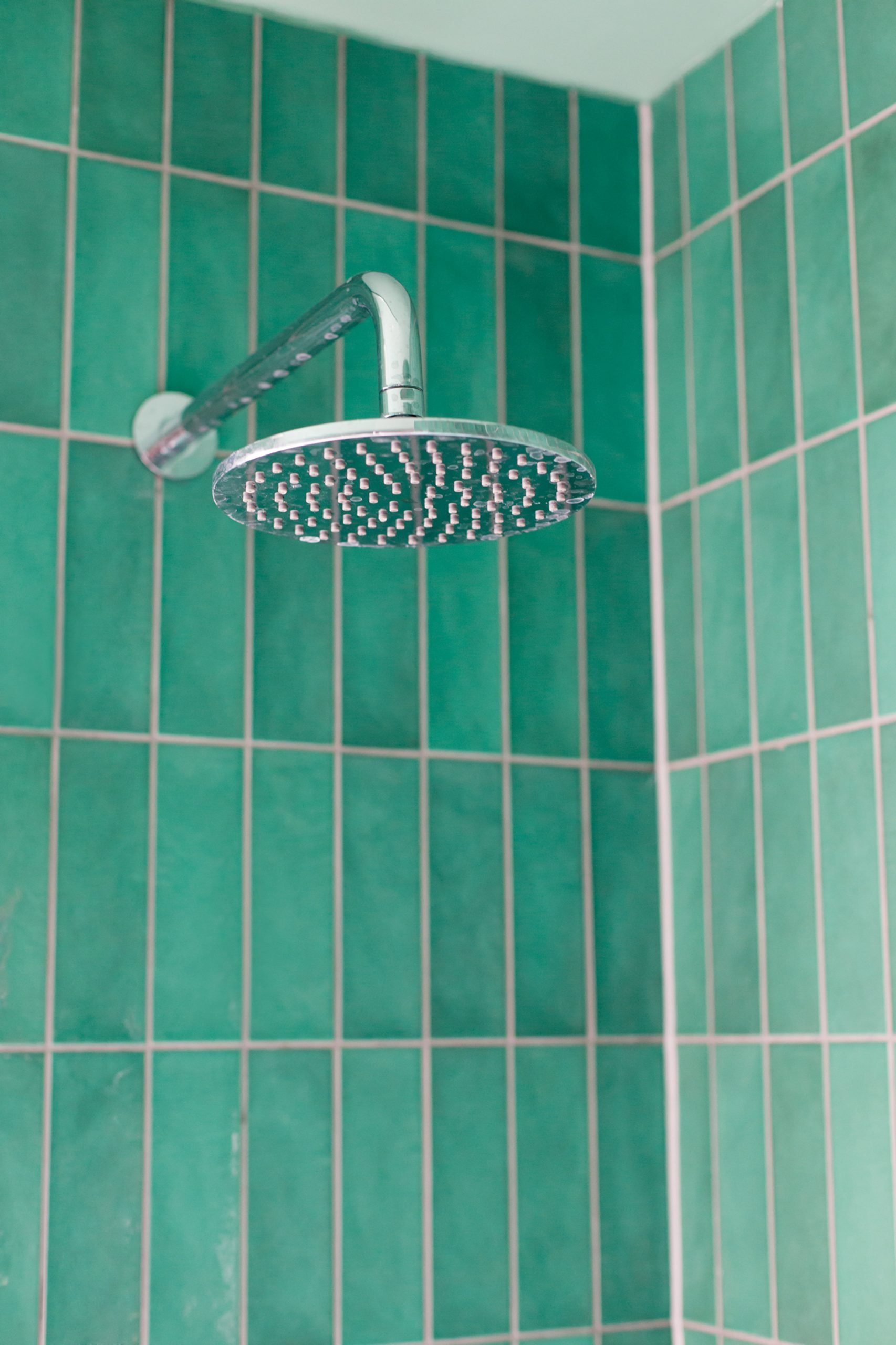 A shower lined with green tiles