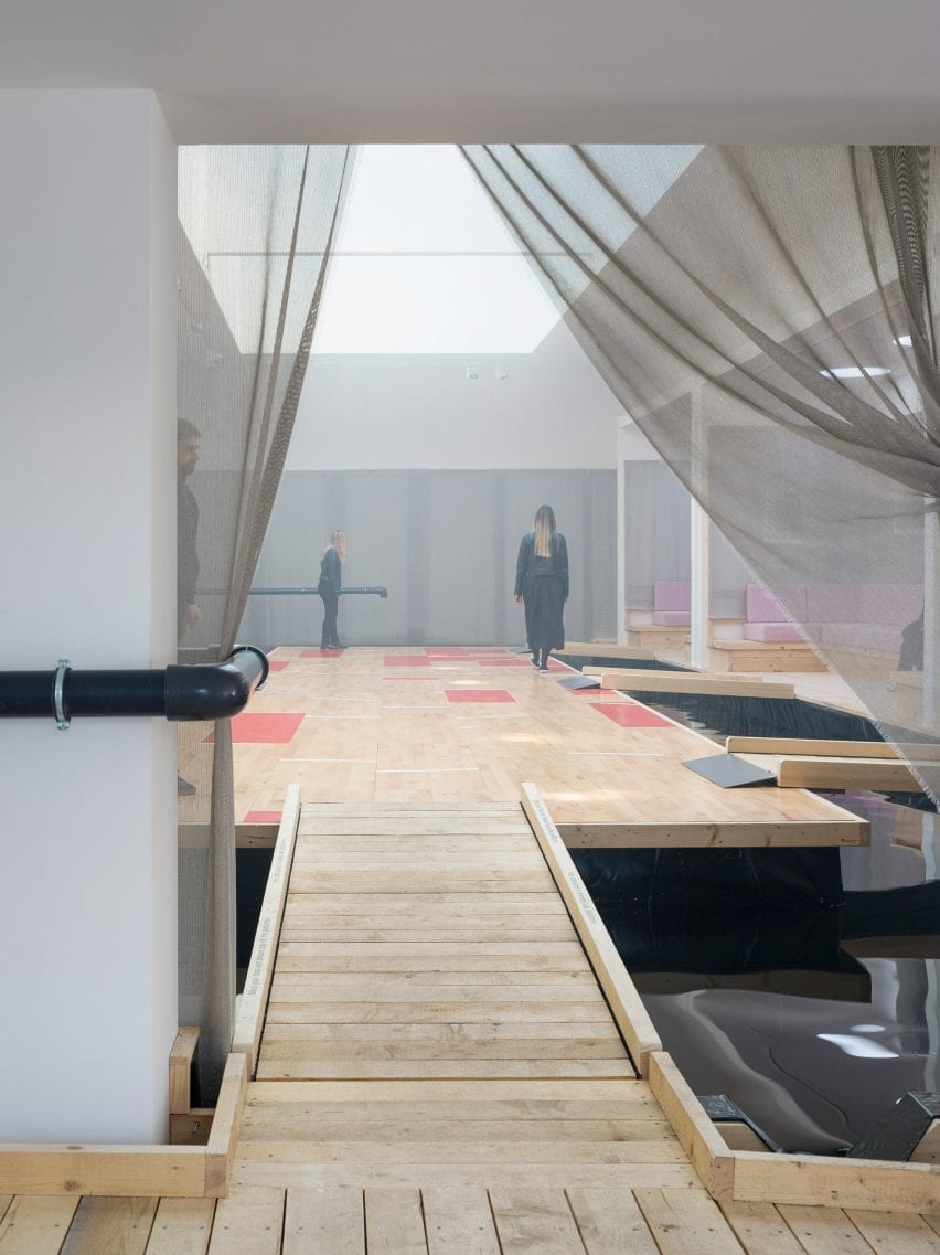 A pine footbridge floats above a flooded room at the Danish Pavilion