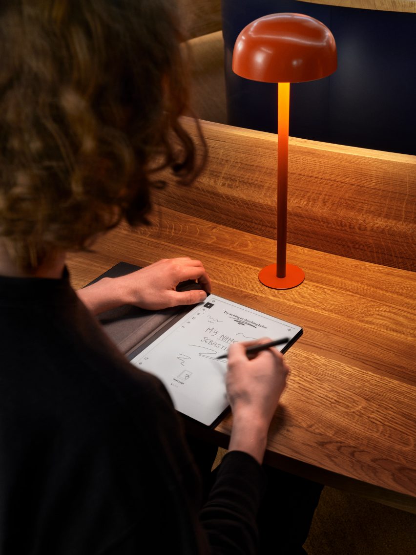 Person writing on reMarkable paper tablet at oak desk