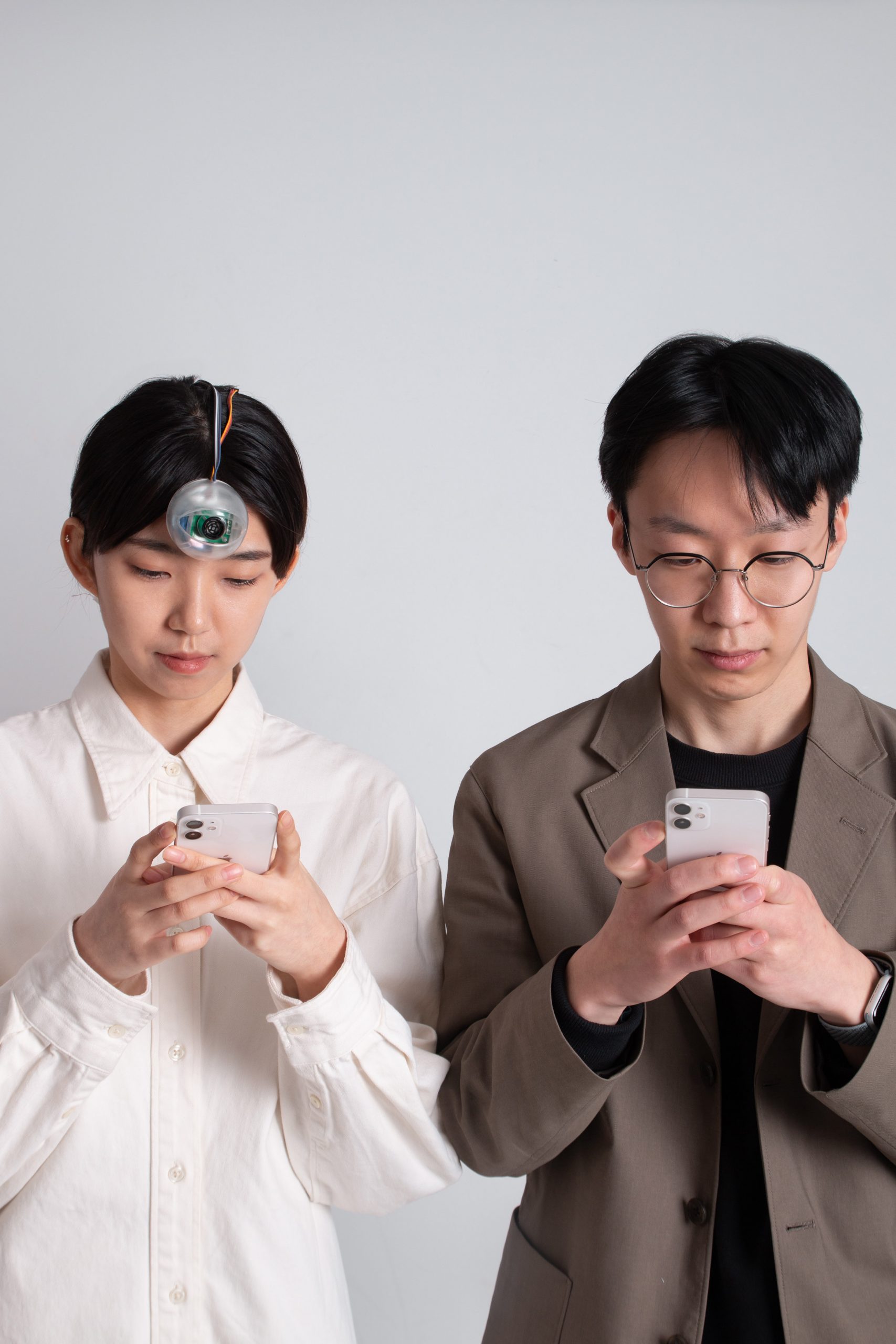 Woman wearing a robotic Third Eye looking at her phone next to man looking at his phone