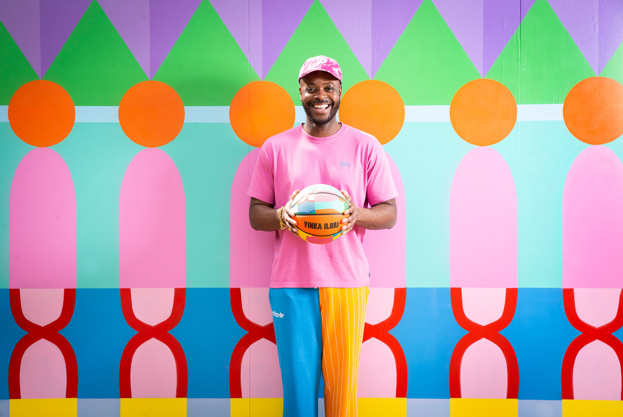 Yinka Ilori holding basketball in front of colourful printed hoarding