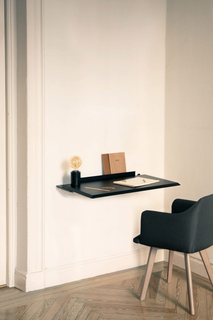 Black version of the Alada desk folded out with stationary and lamp on top 