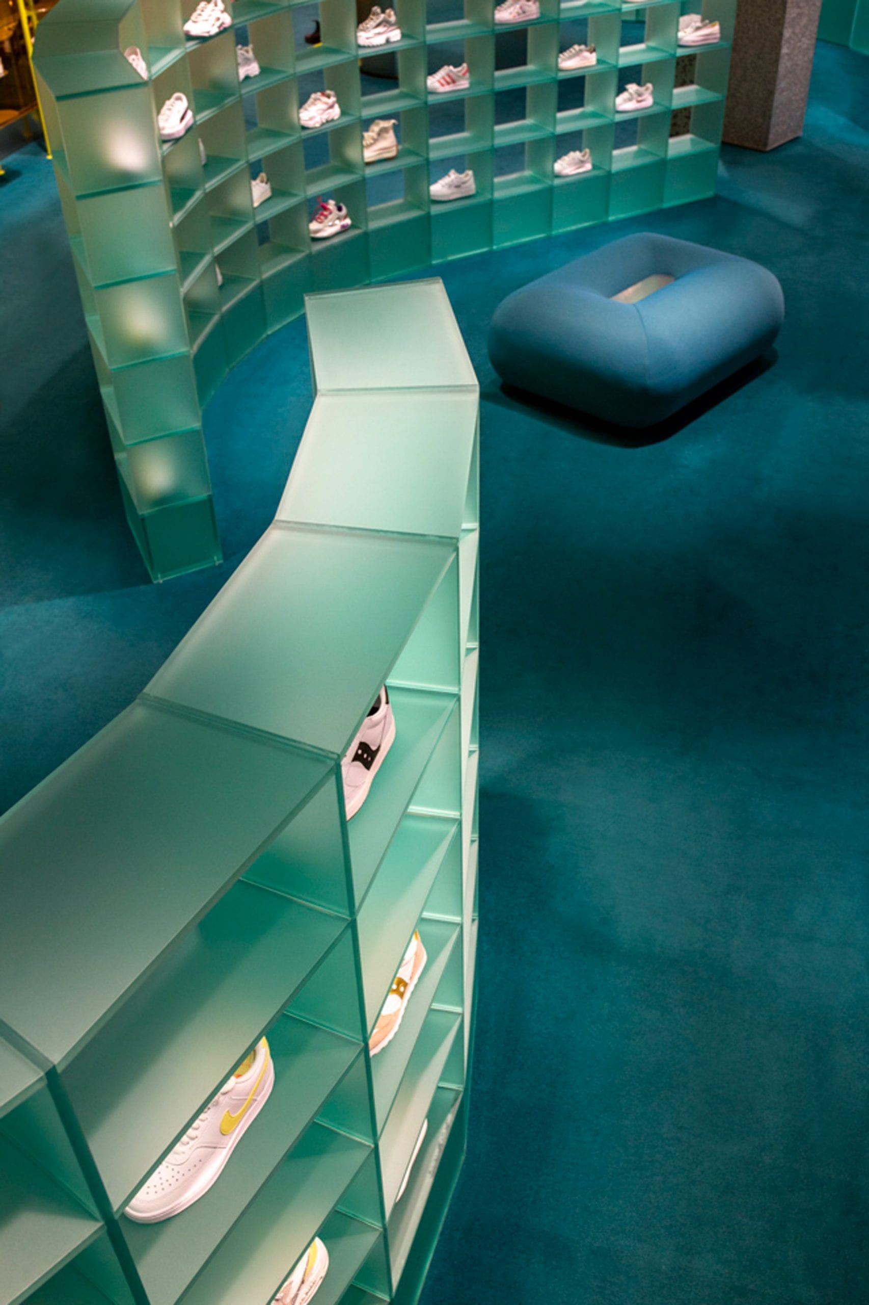 Curved plexiglass shelving displaying trainers on blue carpet in retail interior by Studiopepe
