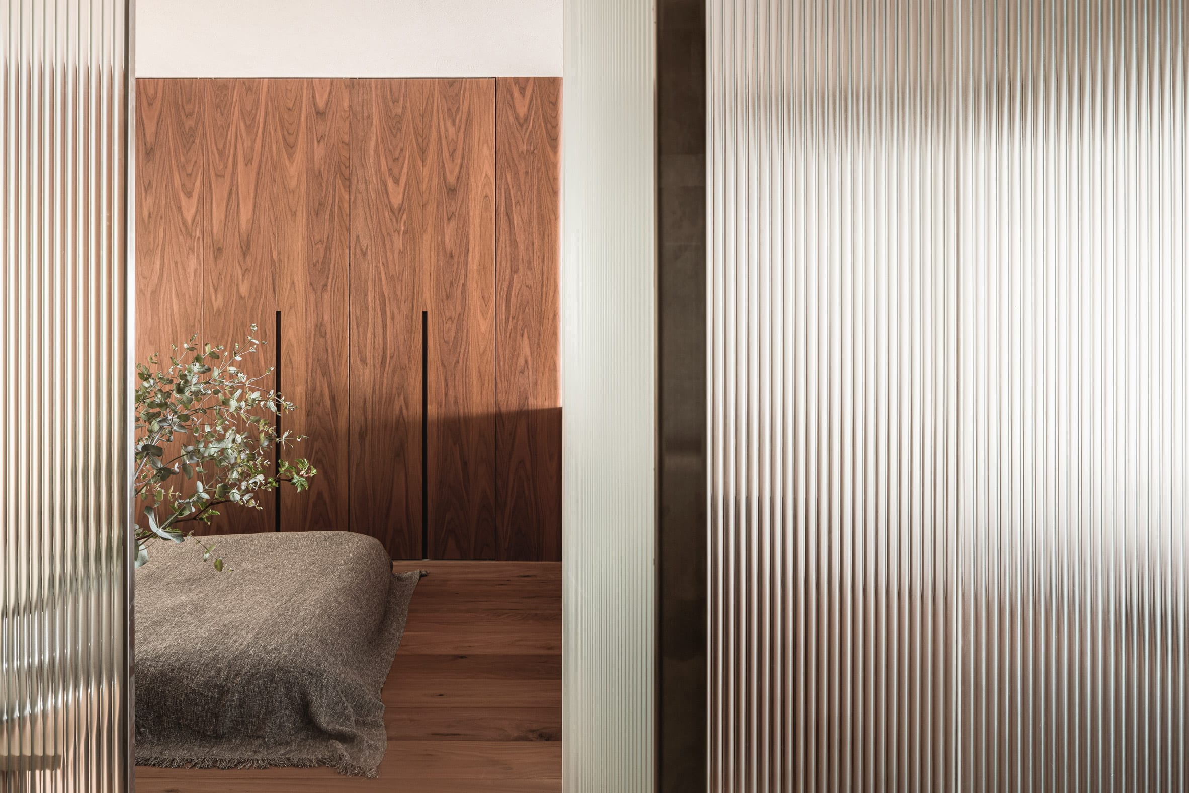 Bedroom with built-in wooden wardrobe and reeded glass partitions in interior by I IN