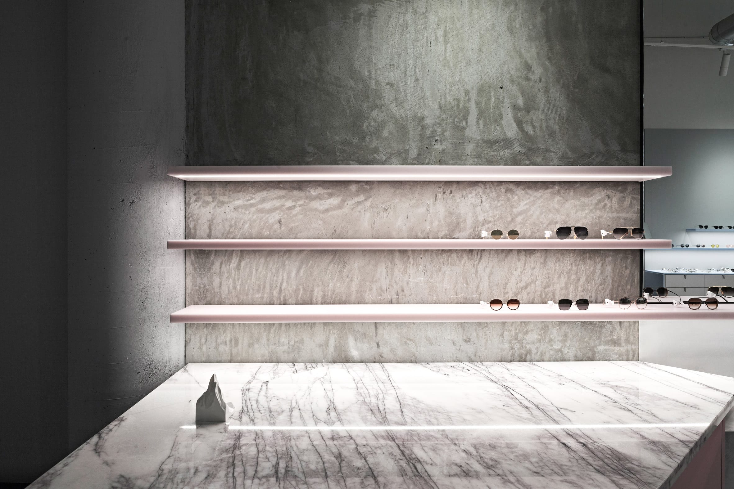 Transluscent pastel pink sunglasses displays with marble counter in retail interior by Studio Edwards