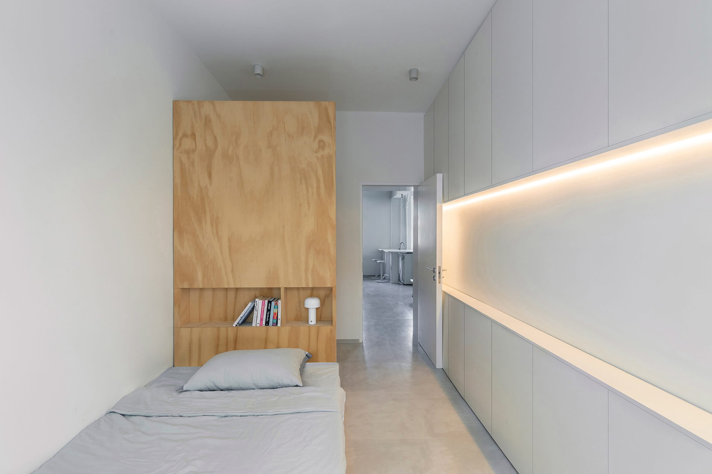 Bed with tall plywood backrest in white-painted room of post-war Beijing apartment