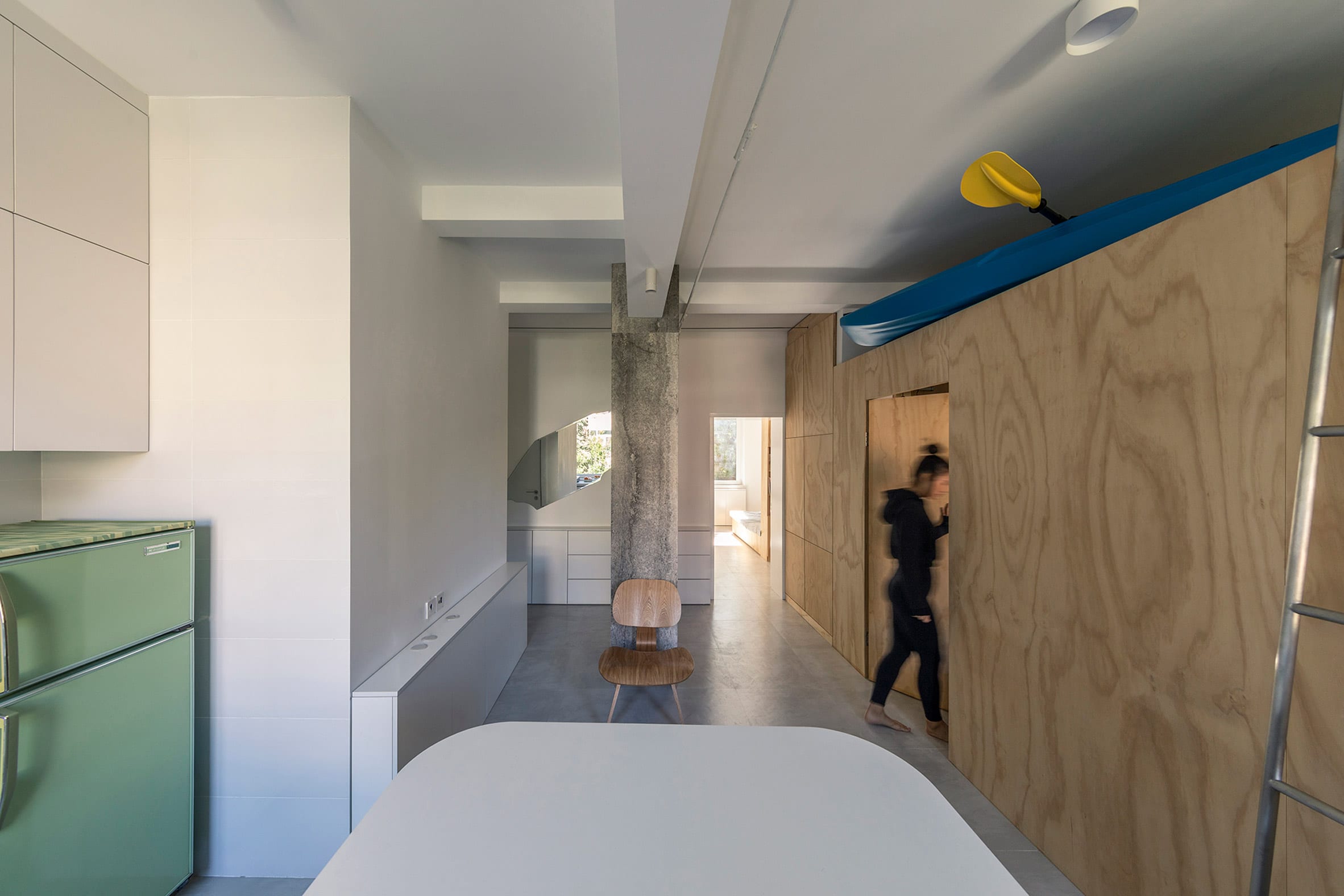 Open-plan room with kitchen and plywood unit holding a kayak in interior by Rooi