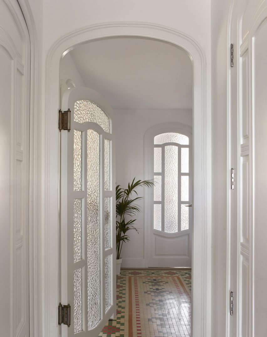 Hallway with curved wooden doors with mottled glass and mosaic floors by DG Arquitecto
