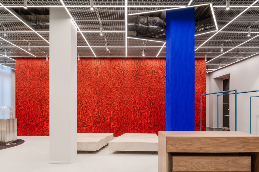 Red patterned wall with blue and white pillars in retail interior by AMO