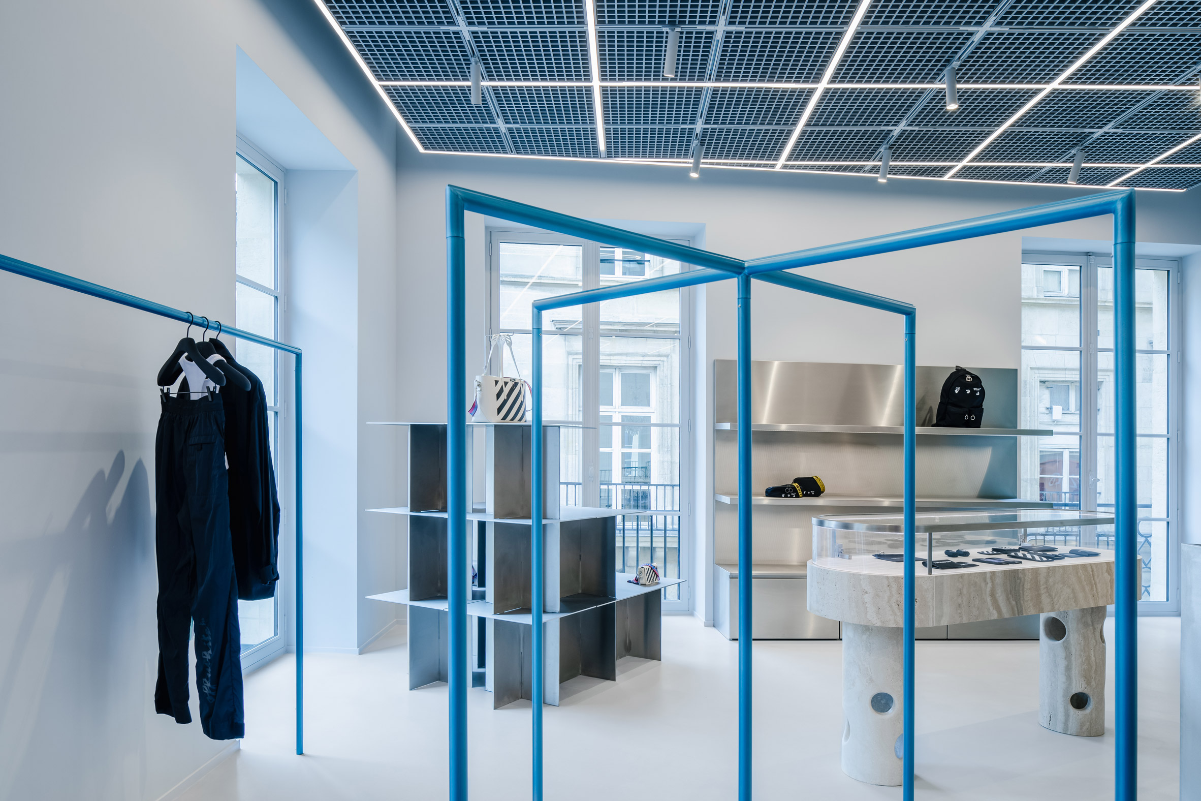 Blue clothes rails and steel displays in retail interior by AMO