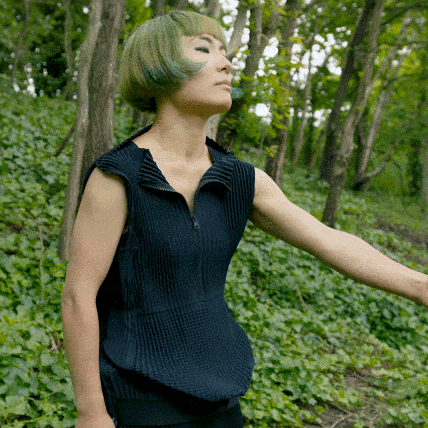 Seorang wanita di hutan hijau membentangkan pakaian Petit Pli-nya