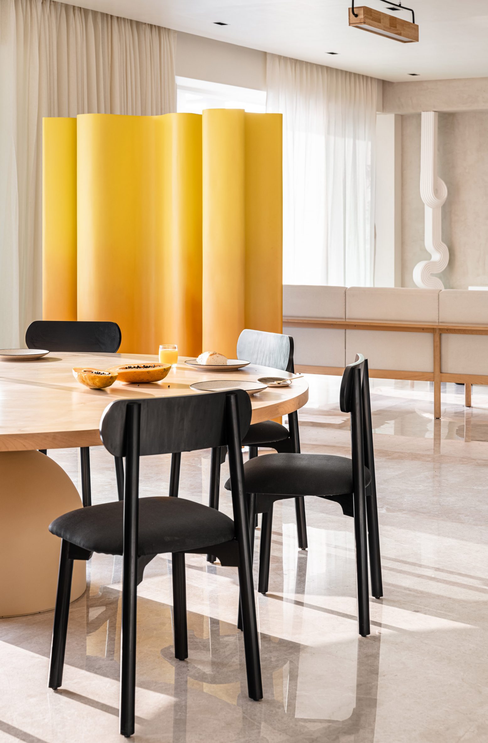 Dining room with wooden table, black chairs and wavy partition wall in yellow by The Act of Quad