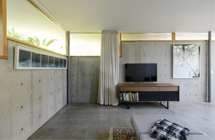 concrete living room with wood framed windows by No Architecture