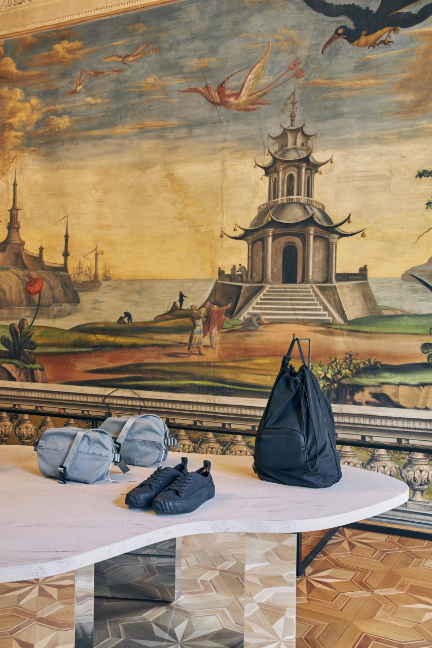 Bolsos y zapatos exhibidos en la mesa de piedra frente al mural