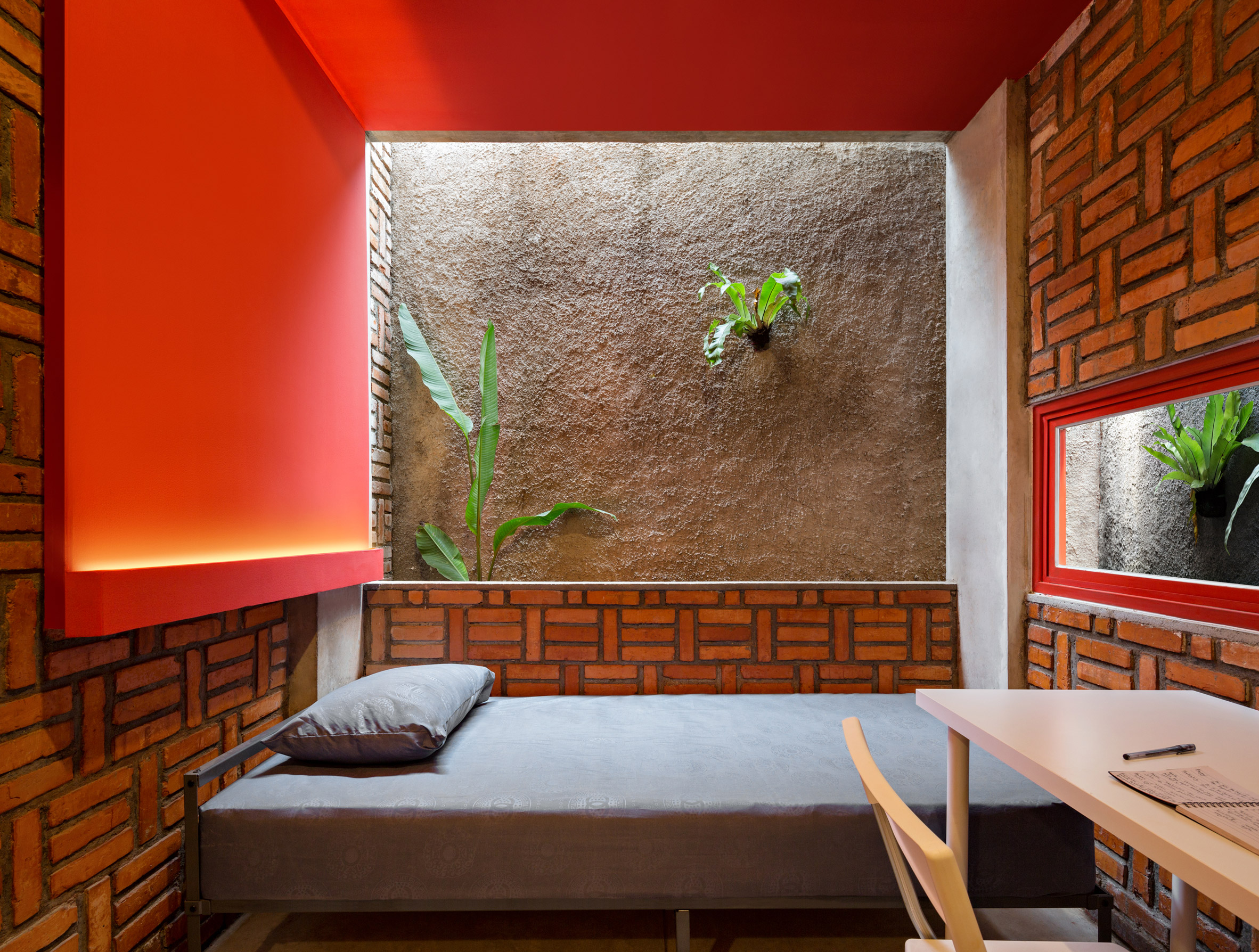 Dormitory room with walls showing a contrast of red paint, brickwork, concrete and greenery