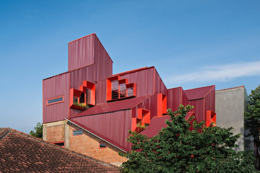 Red stacked boarding house volumes rise above the surrounding rooftops