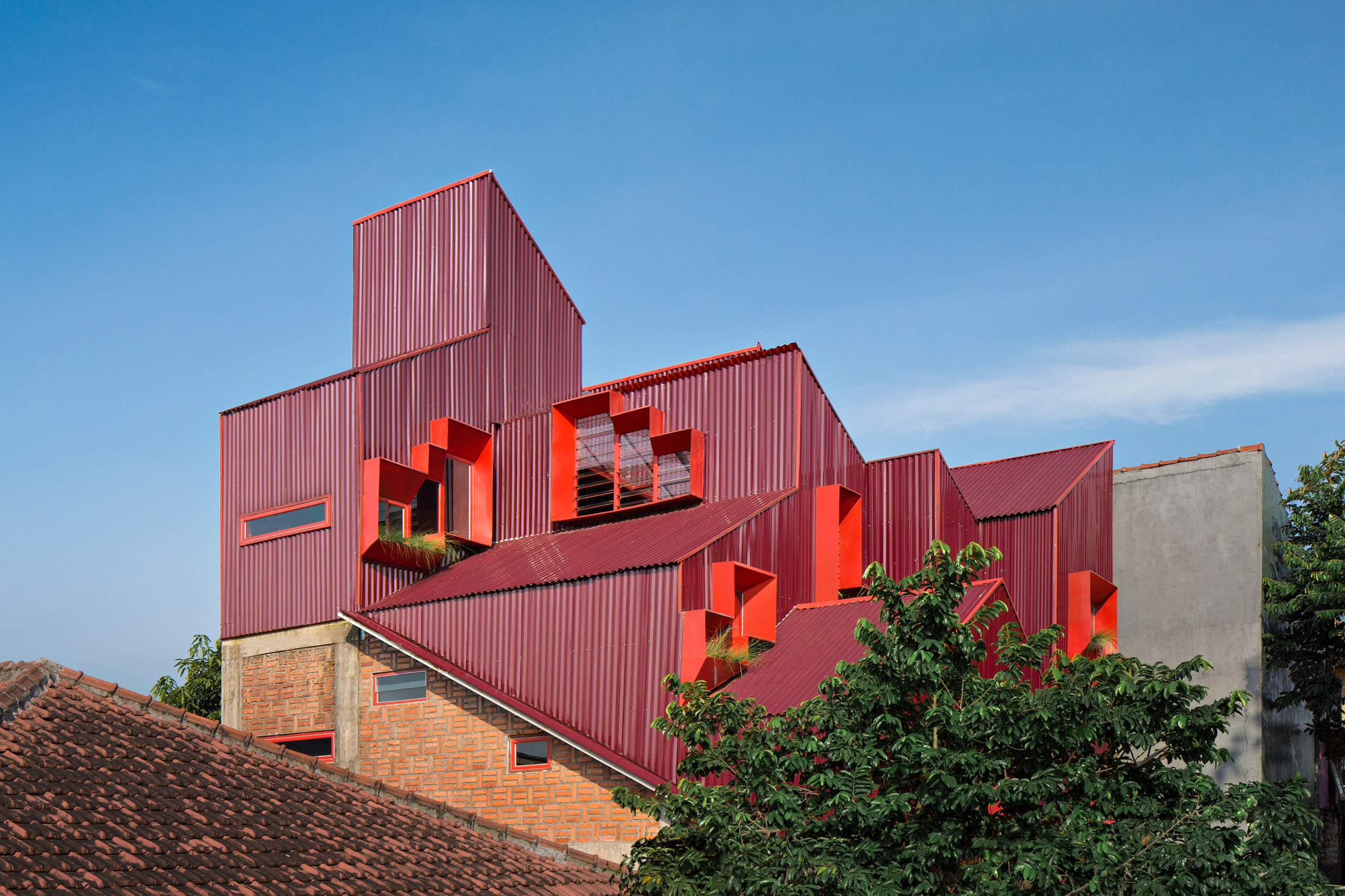 Red stacked boarding house volumes rise above the surrounding rooftops