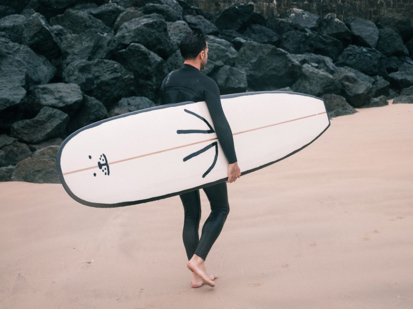 A surfer carries the seal surfboard across a beach