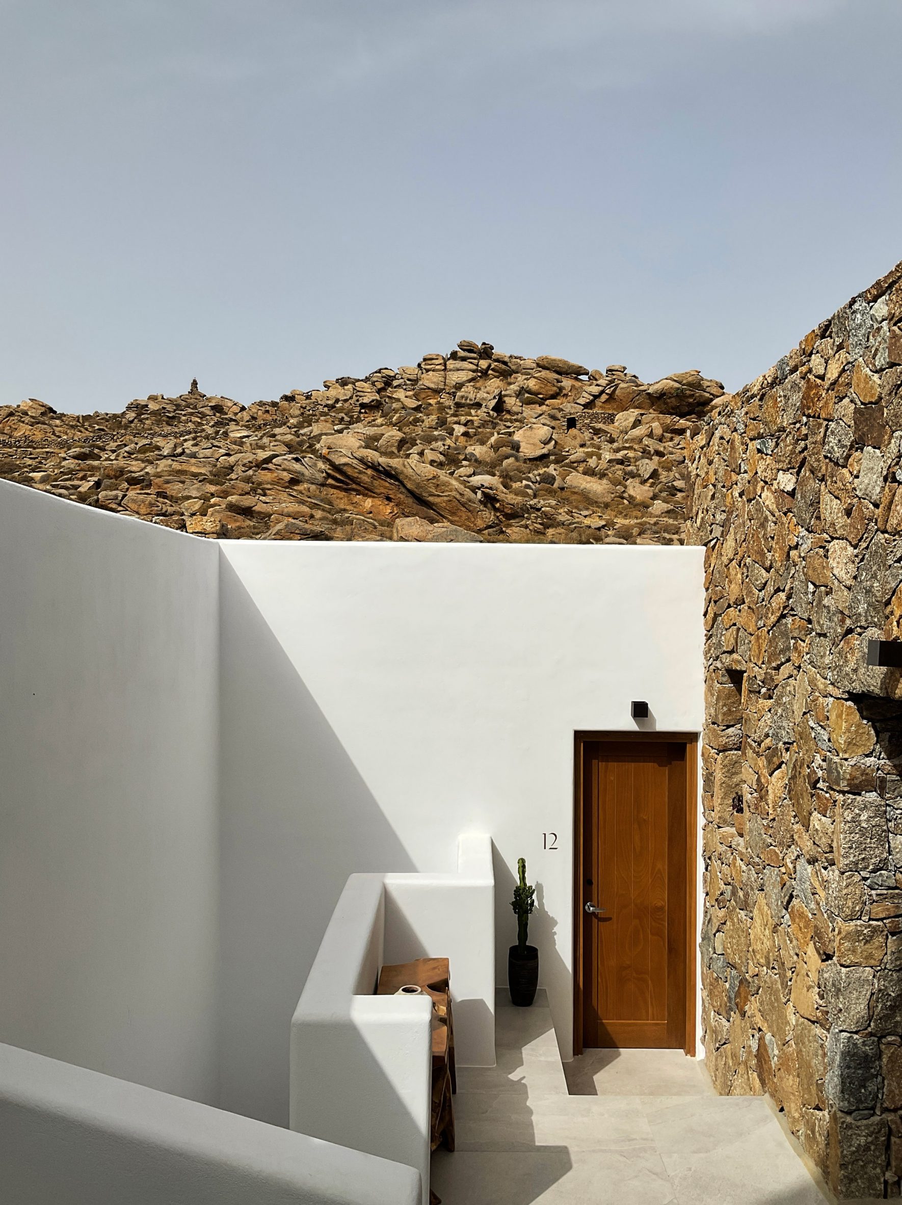 Entrance to Mykonos Wellness Resort with one whitewashed wall and one stone one that blends into the hill