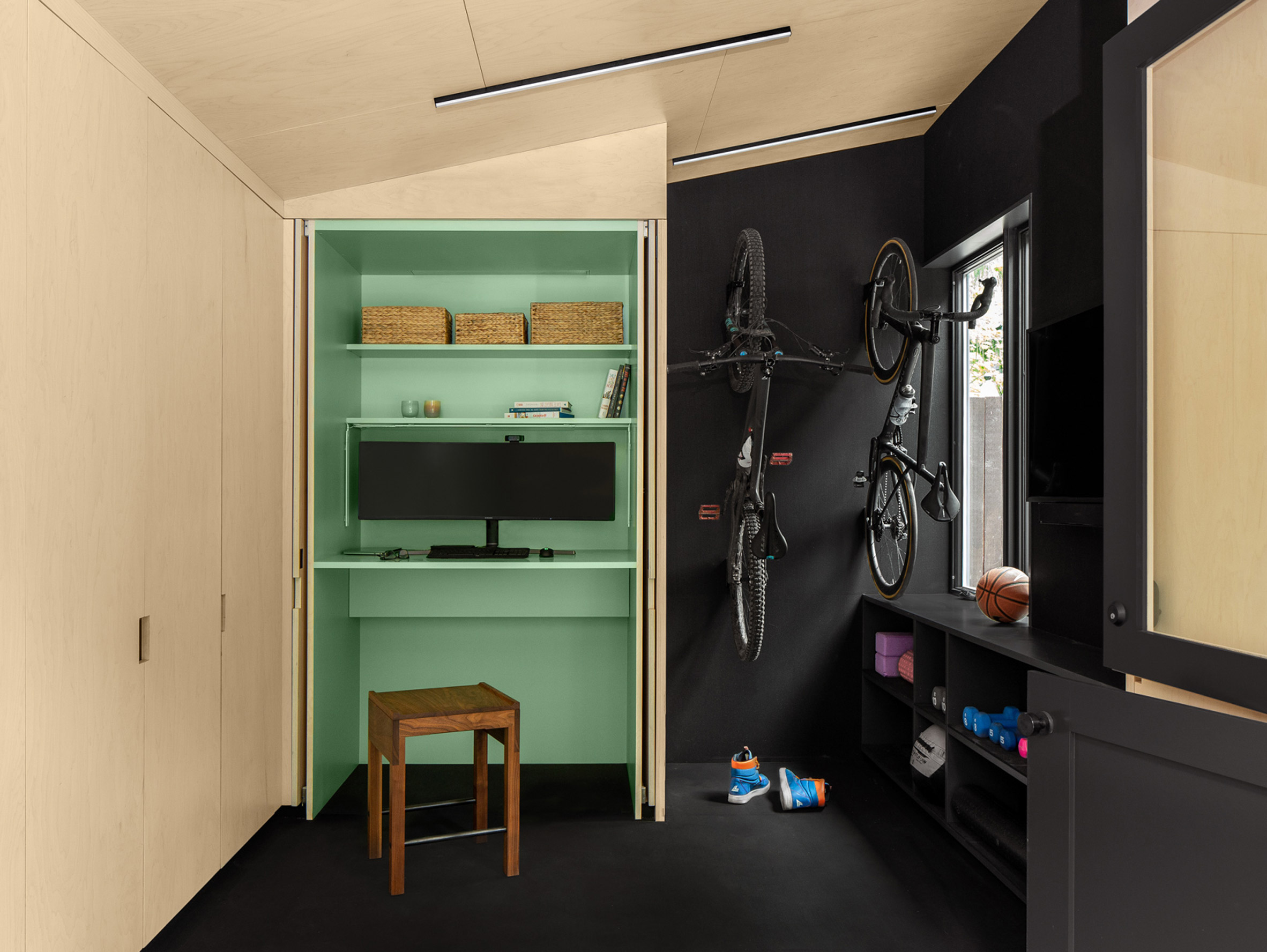 A sea-green coloured built in desk and bikes hanging on the wall
