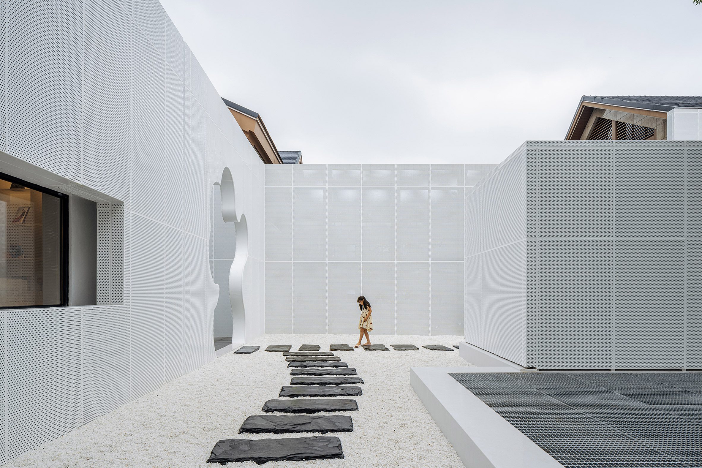 Courtyard with white pebbles surrounded by perforated white aluminium facade by Wutopia Lab